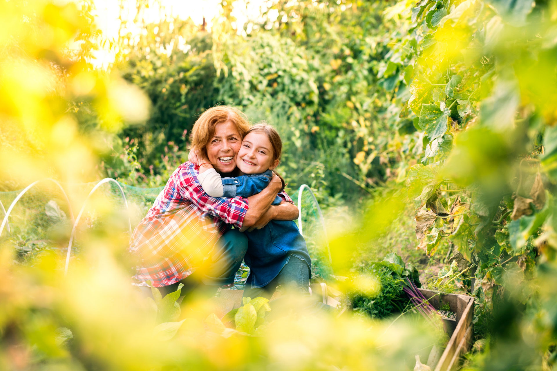 A smiling lady hugs a happy young girl while on an allotment harvesting vegetables.