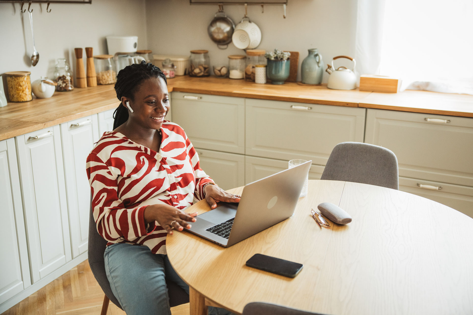 Young pregnant woman having a video call on her laptop on the kitchen table