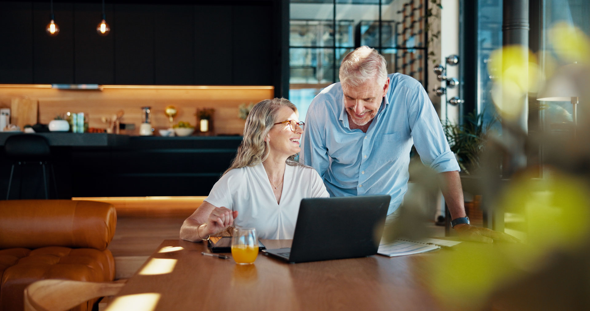 A happy older couple smiling together at a laptop on a dining table