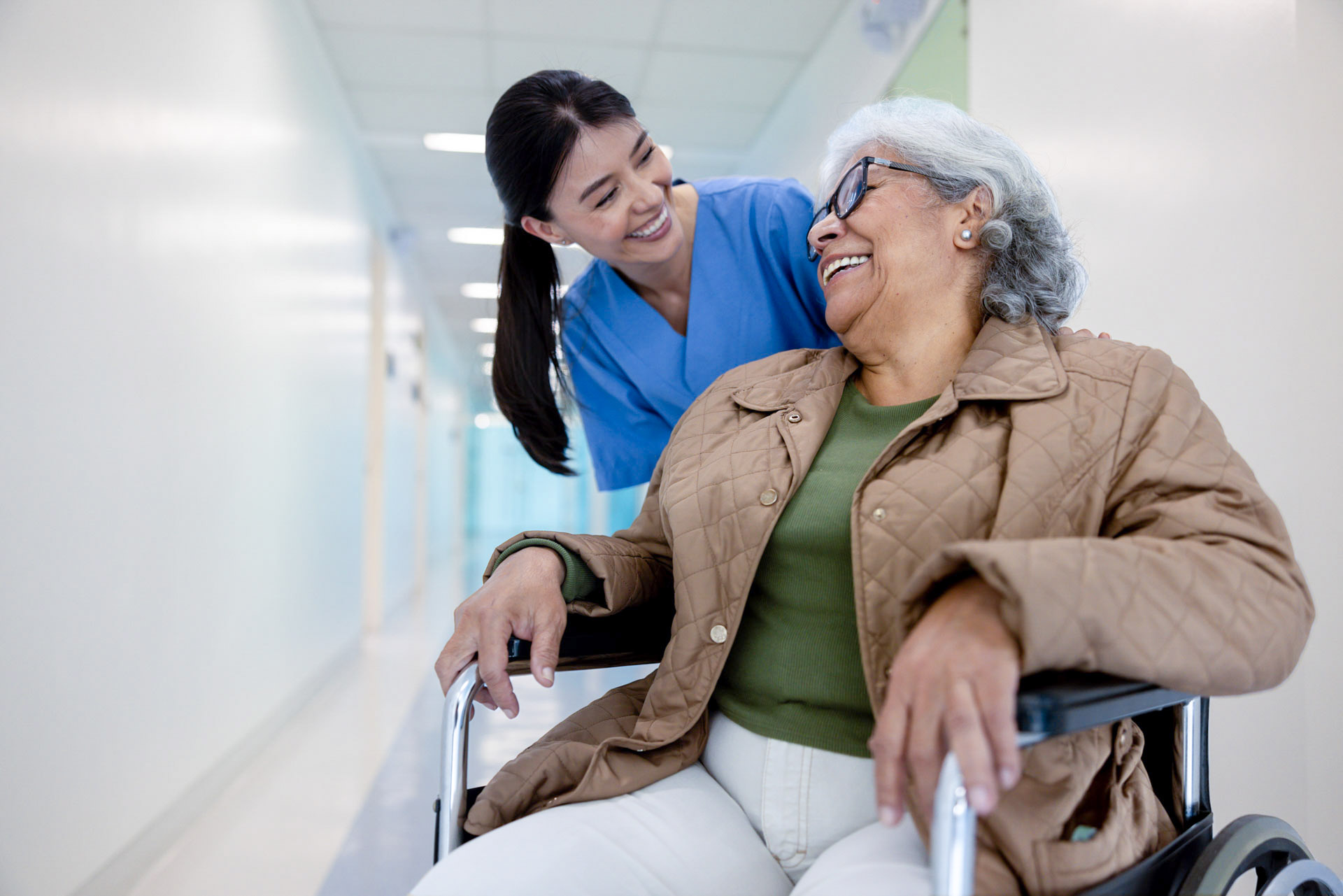 Happy nurse pushing a senior woman in a wheelchair and laughing together at the hospital