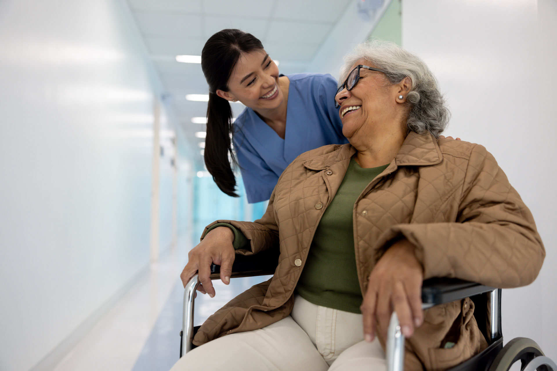 Happy nurse pushing a senior woman in a wheelchair and laughing together at the hospital