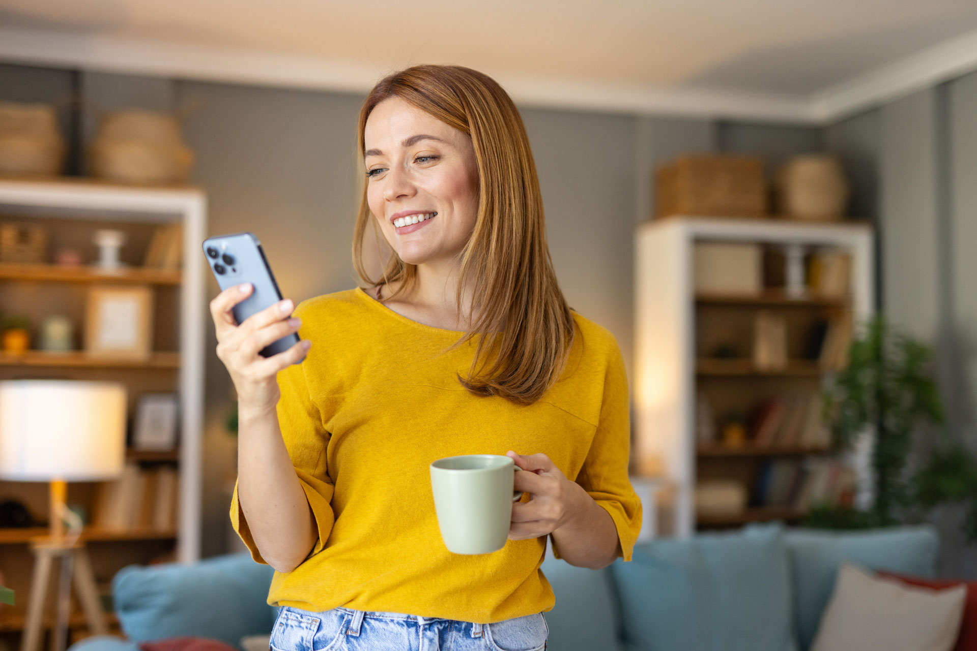 The woman joyfully uses the HBS Platform on her smartphone with a warm mug in hand