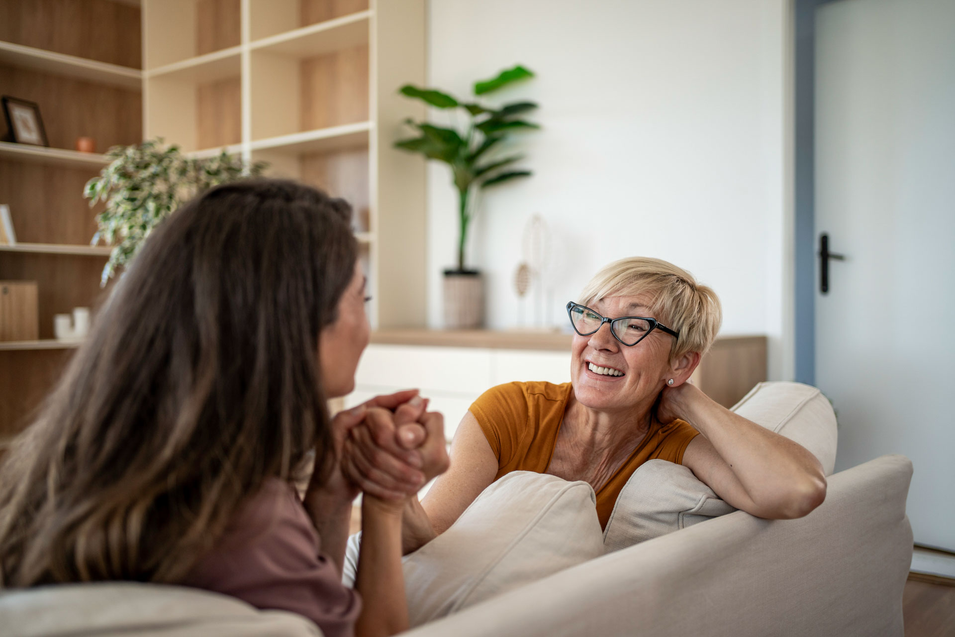 Mother and daughter relax on a sofa, smiling and engaged in warm conversation