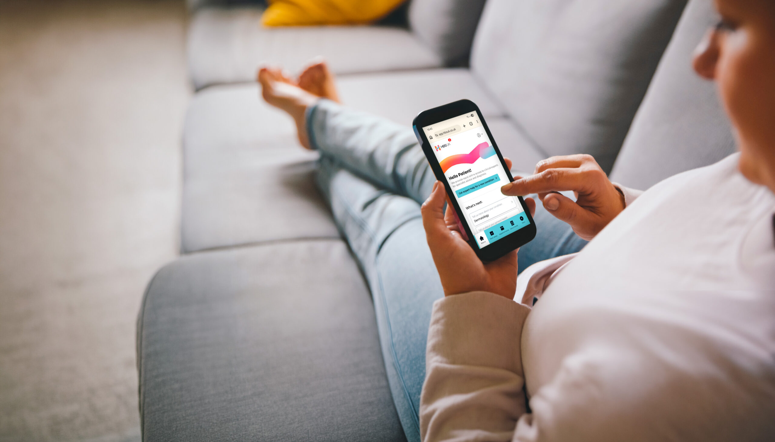A woman uses the HBS Platform on her smartphone while relaxing on her sofa at home