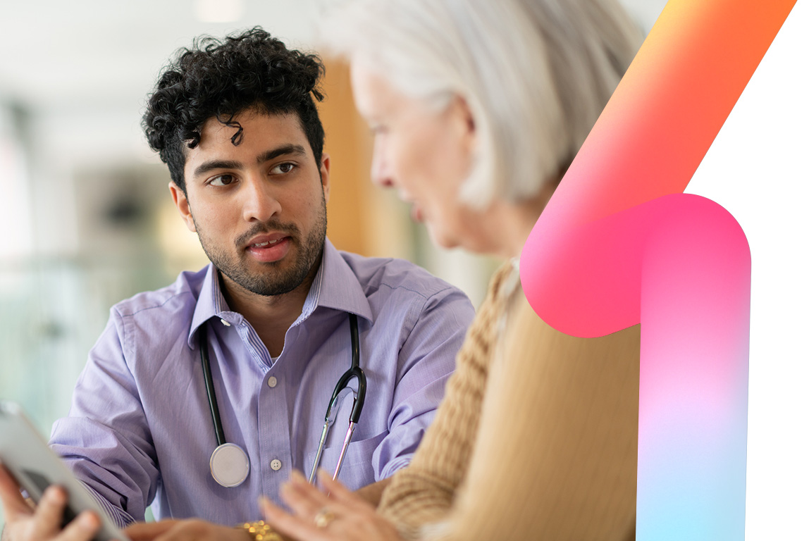 A multiracial doctor is doing a routine check-up with his elderly Caucasian female patient. They are seated at a table together and the doctor is holding a tablet computer. The two are reviewing test results and discussing a treatment plan. The patient is asking a question.