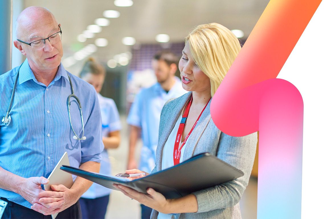 a business woman chats to a doctor in a busy hospital corridor