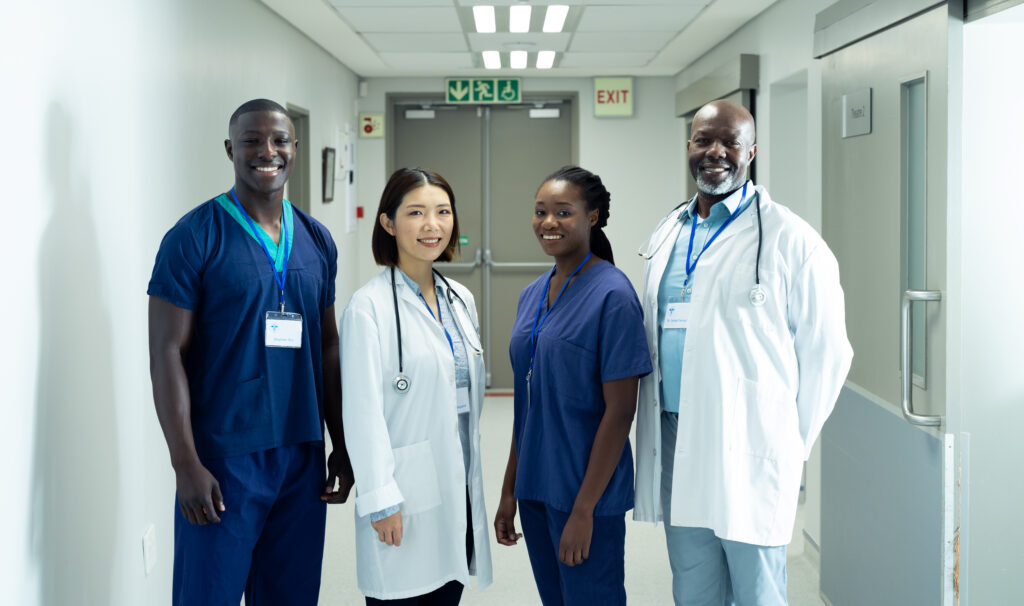 Portrait of diverse group of four doctors and healthcare workers smiling in hospital corridor. Hospital, medical and healthcare services.